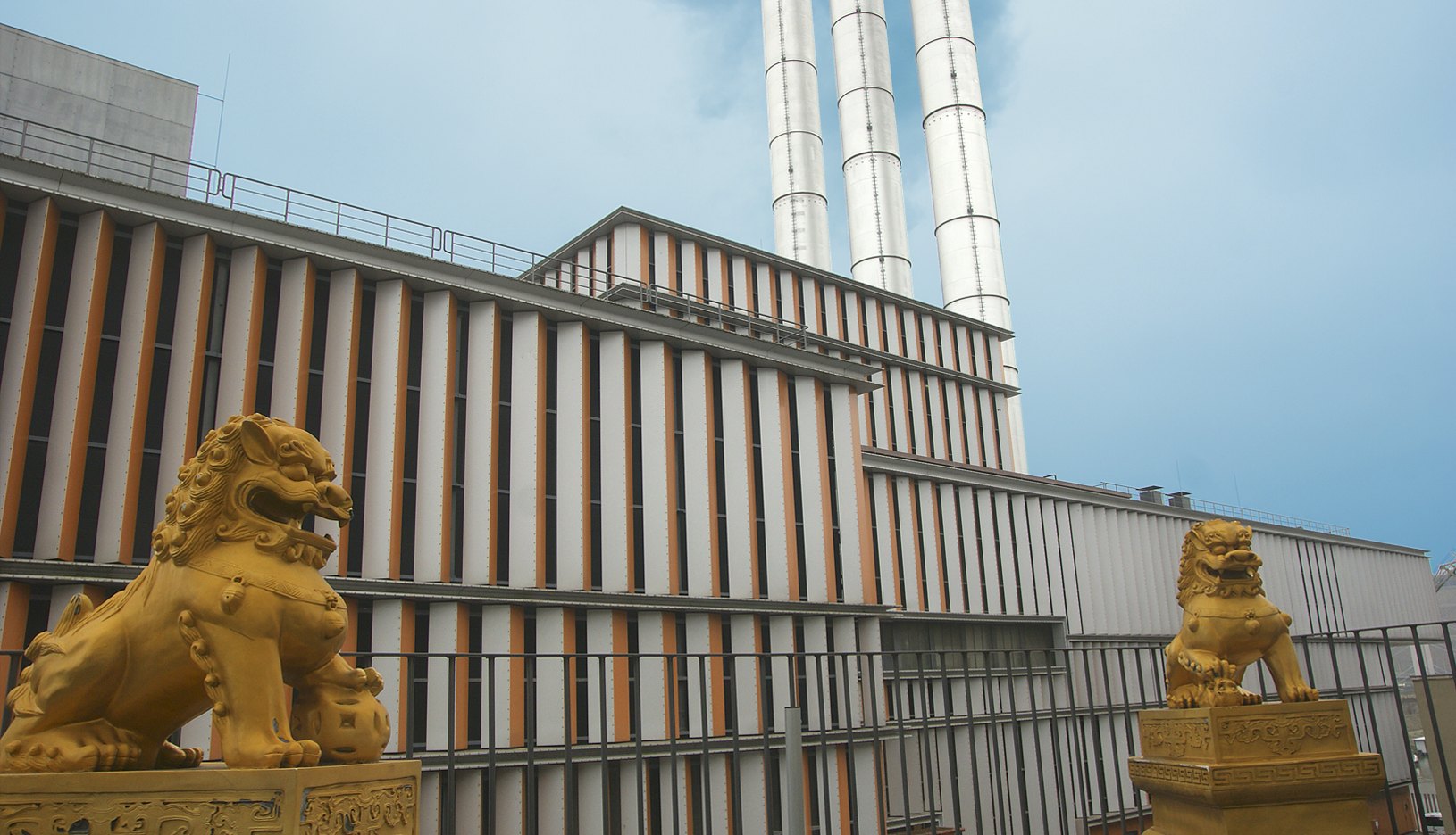Fassade eines Gebäudes mit drei Schornsteinen und zwei goldenen Löwenfiguren im Vordergrund